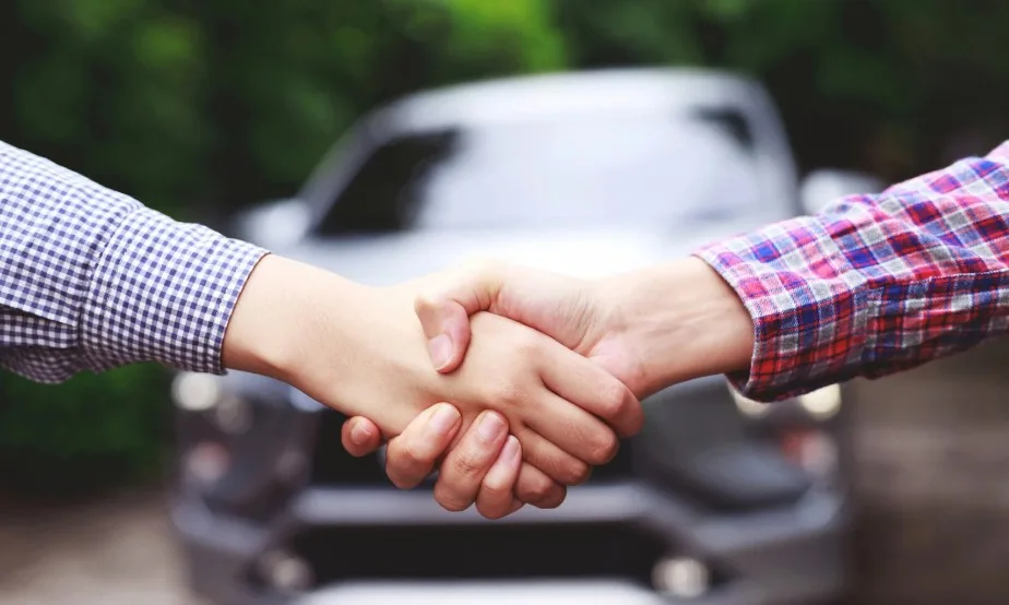 Handshake in front of a car, symbolizing vehicle sales and potential Lemon Law agreements, 247lemonlaw
