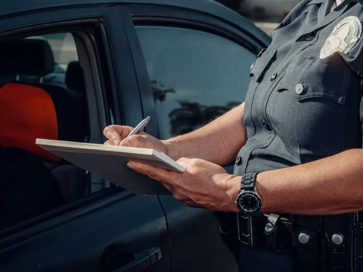 Police officer writing a citation beside a vehicle during a traffic stop.