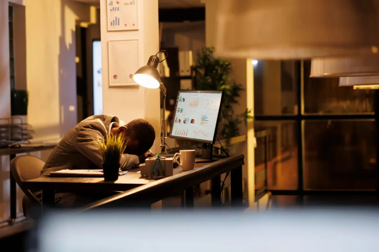 Tired worker sleeping at his desk during late hours, showing the harmful effects of workplace fatigue.