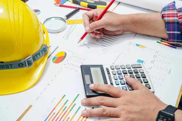 Construction worker calculating project costs and labor pay using charts and calculator