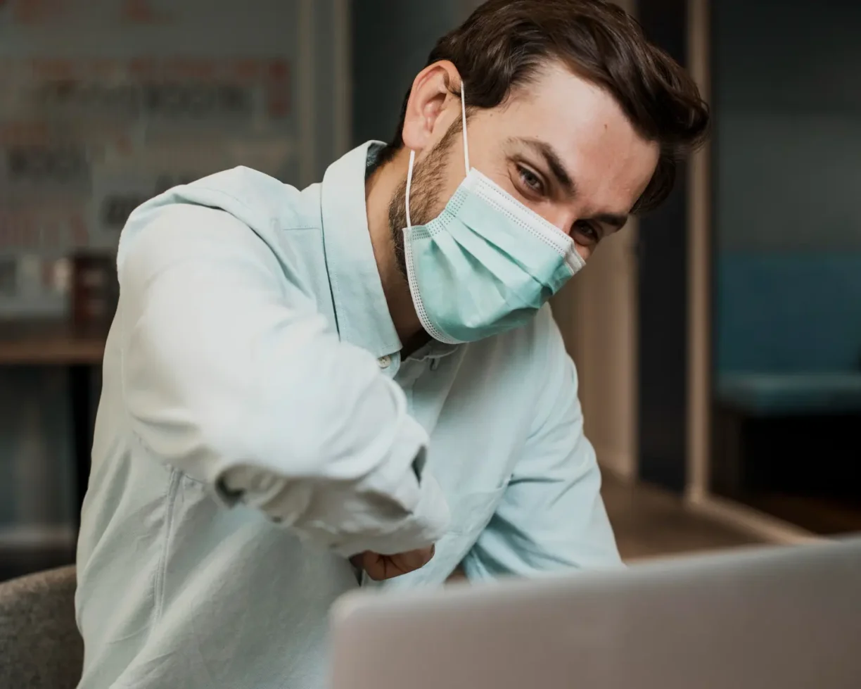 Employee wearing a face mask while working on a laptop, highlighting illness prevention and workplace health safety.