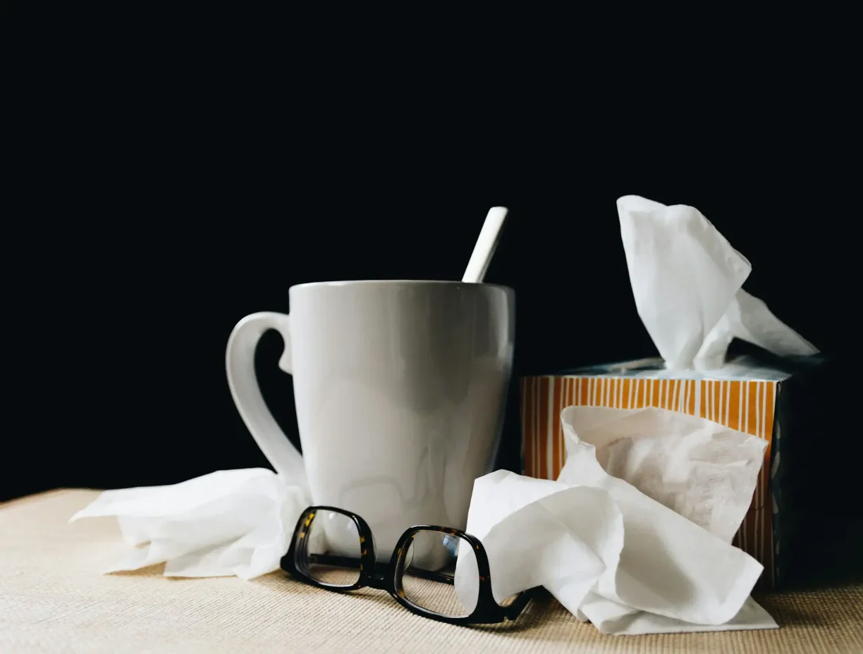 Hot drink, tissues, and eyeglasses on a table, symbolising cold, flu symptoms, or illness recovery.