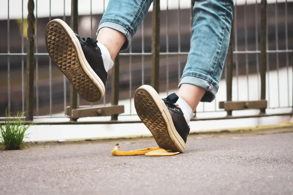 A person wearing jeans and sneakers slipping on a banana peel, a classic example of a premises liability accident requiring hiring a personal injury lawyer.
