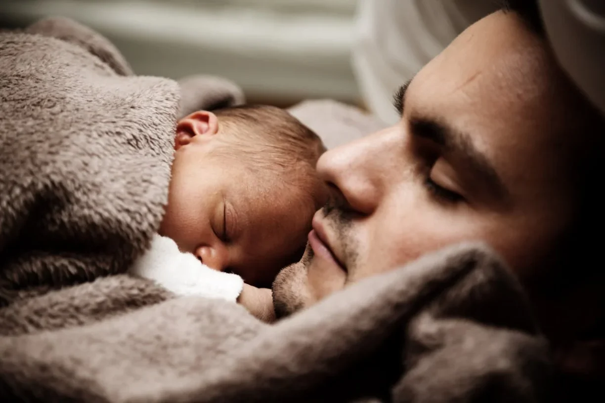 Father and newborn sleeping together during bonding time protected by california paternity leave laws