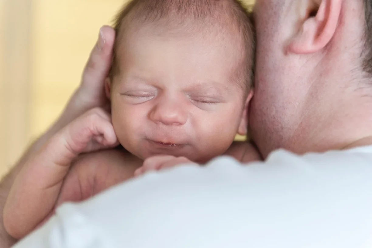 New father holding newborn on shoulder during paternity leave in California